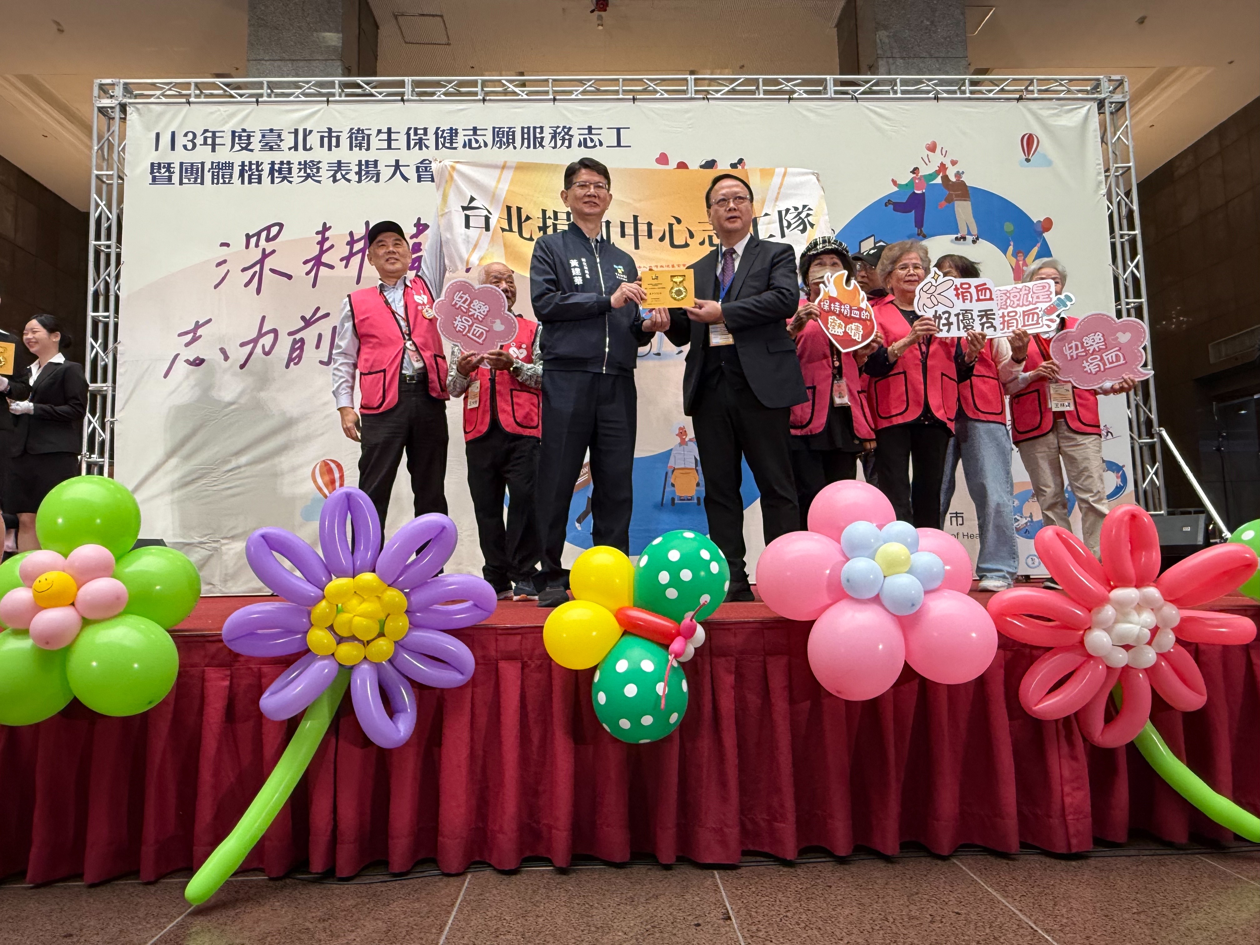 台北捐血中心志工團隊榮獲台北市衛生局113年度衛生保健志願服務志工團體楷模表揚，中心主任林敏昌代表(右)上台受獎並與臺北市政府衛生局黃建華局長(右)合影留念。